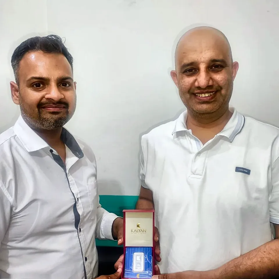 A ProperPaisa advisor handing a Kalyan Jewellers 999 silver coin to a customer after their loan was disbursed